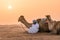 Wahiba Sands,Oman - 04.07.2018: A man in white robe and his camel sit on the desert sand. Early morning in Wahiba Sands