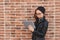 Waist portrait of young woman standing in the street beside brick wall, listening music online with headphones from