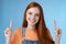 Waist-up charismatic good-looking european redhead woman smiling sincere gladly showing way pointing up index fingers