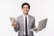 Waist-up of happy, pleased smiling young asian man in grey suit holding dollars, getting rich, using laptop as