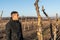 Waist up photo of the young man gardener in black clothes stands among his old apple garden and looking at the sawed