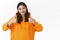 Waist-up portrait asian millennial girl in orange hoodie showing thumbs-up in like or approval, smiling acceptingly