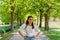 Waist-up portrait of beautiful young woman standing on avenue of trees in park during spring