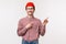 Waist-up portrait of curious excite geeky adult man in red beanie, checked shirt, pointing and looking upper right