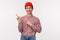 Waist-up portrait of happy smiling geeky guy in glasses and red beanie, pointing and looking upper left corner with