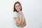 Waist-up shot of friendly-looking joyful lucky girl with brown short haircut standing in profile holding hand on cheek