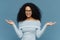 Waist up shot of happy young crisp Afro American woman raises both hands, pretends holding something, wears blue sweater, has