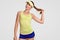 Waist up shot of self confident beautiful healthy tennis player holds pony tail, dressed in sportswear, poses against white studio