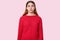 Waist up shot of surprised European woman with long straight hair, raises eyebrows, dressed in red pullover, reacts on astonishing