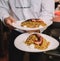 Waiter in a fancy restaurant carrying two gourmet plates of rice with octopus tentacle