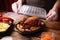 Waiter in gloves closing container with fresh prepared meal at wooden table, closeup. Food delivery service