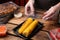 Waiter in gloves closing container with grilled corn cobs at wooden table, closeup. Food delivery service