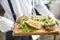 The waiter is holding a plate Beef bone marrow with chimichurri sauce and toasted bun. Served on a chopping wooden Board