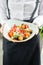 The waiter is holding a plate Traditional greek salad with fresh vegetables, feta cheese and olives. Wooden table in