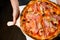 Waiter holds serving board with delicious pizza with chicken meat, olives, mushrooms, sause and cheese