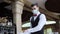 A waiter in a medical protective mask serves the table in the restaurant