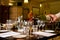 Waiter`s hand pours white wine into a wineglass while a sommelier woman explains during wine testing