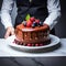 Waiter serving Chocolate cake on a white plate with ganache, cream and fruit