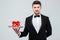 Waiter in tuxedo with bowtie holding present box on tray