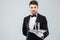 Waiter in tuxedo holding glass of water on metal tray