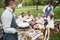 Waiters serve group of good friends that sit outdoors on the beautiful field with trees