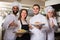 Waitress and crew of professional cooks posing at restaurant