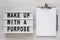 `Wake up with a purpose` words on a lightbox, clipboard with blank sheet of paper on a white wooden surface, top view. Overhead,