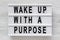 `Wake up with a purpose` words on a modern board on a white wooden background, top view. Overhead, from above, flat lay. Close-u