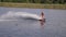 Wakeboarder man holds rope handle and rides on board on river in slow motion with water splashes on background of reeds