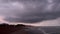 Walking along a sandy ocean shore under grey storm clouds in morning twilight. POV view of seaside promenade.