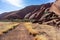 Walking path to Mount Uluru, sacred aboriginal mountain. Dry vegetation on the sides. Rocks and stones on the conglomerate wall of