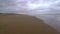 Walking in the sand of an empty lonely beach during a cloudy day, bordering the sea waves