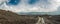 Walking tourist on a dirt road leading to green hills among black lava and dramatic cloudy sky. Panoramic view of the slopes of