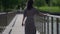 walks at summer, adult woman is strolling over bridge, rear view, dark hair are swaying by wind