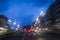 A walkway and a car on a night street, lit by the shrubs and blurred shadows.