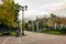 Walkway in the city`s public Park. Beautiful white metal arch, lots of greenery, trees and conifers around, lawn grass along the e