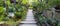 The walkway is paved with concrete slabs and gravel. Surrounded by a variety of tropical rainforest plants. Panorama