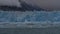 A wall of blue ice with sharp spikes rises above a turquoise lake.