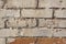 A wall of bricks has clear signs of the effects of time and natural elements, crumbling cement mortar, soiled paint