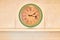 Wall clock on brown background and copy space. Shelf with frames from paintings. Green and beige color of the clock with Roman