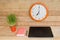 Wall clock, laptop, notebook and pen. Home workplace. Green houseplant on the table. Wooden background