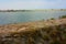 Wall on the edge of a path beyond which the river water flows into the sea in summer between sand and sky