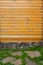 Wall of house is made of worn lining boards with many knots, a basement and a path of stones with grass below.