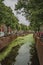 Walled canal with aquatic greenish plants, brick buildings and clouds at Gouda.