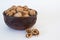 Walnuts lie in a bowl, chopped nuts nearby, on a white background
