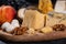 Walnuts lie next to a large piece of Parmesan cheese, other types of cheese, and fruits. An exquisite appetizer for an