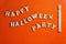 Wand in the form of a mummy and the inscription HAPPY HALLOWEEN PARTY made of wooden letters. Bright orange background. Copy space