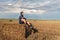 A wandering guy in a hoodie in a hood sits on a haystack in a wheat field with a backdrop of a sunset stormy sky