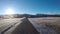 Wandering on long dirt road towards mighty forest opening with frozen field on each side in late autumn sunshine