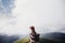 wanderlust and travel concept. girl traveler in hat with backpack looking at clouds in mountains. stylish hipster woman exploring